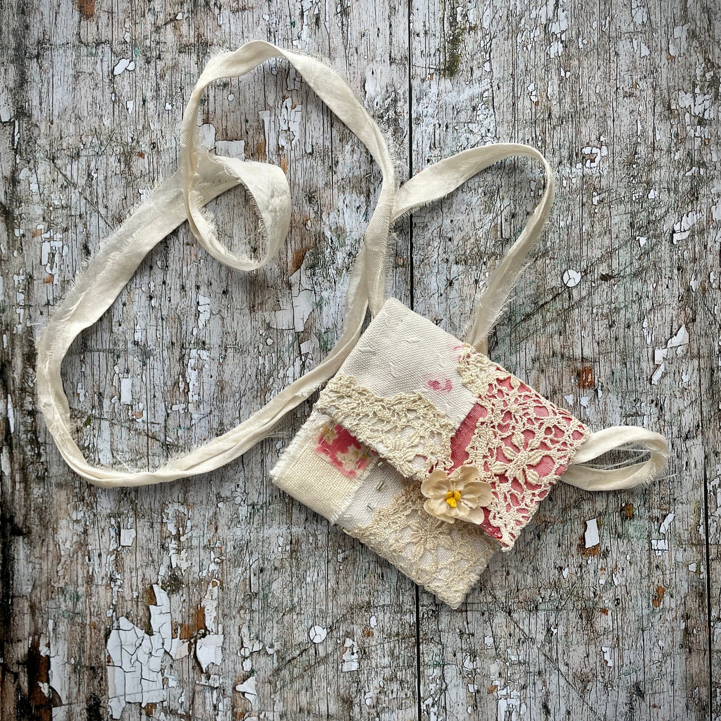 Small Hand Stitched Vintage Fabric Pouch
Beautifully hand stitched pouch to hold your precious memories... a photograph, crystals, a talisman or finds from the beach. It has been made by slow stitching together vintage French linens, lace, silk and quilting fabrics in shades of cream and white, lined with a pretty pink vintage paisley cotton, then embellished with small silver bugle beads and a vintage fabric flower. The pouch has a simple fold over top, with a raw edged cream sari silk cord