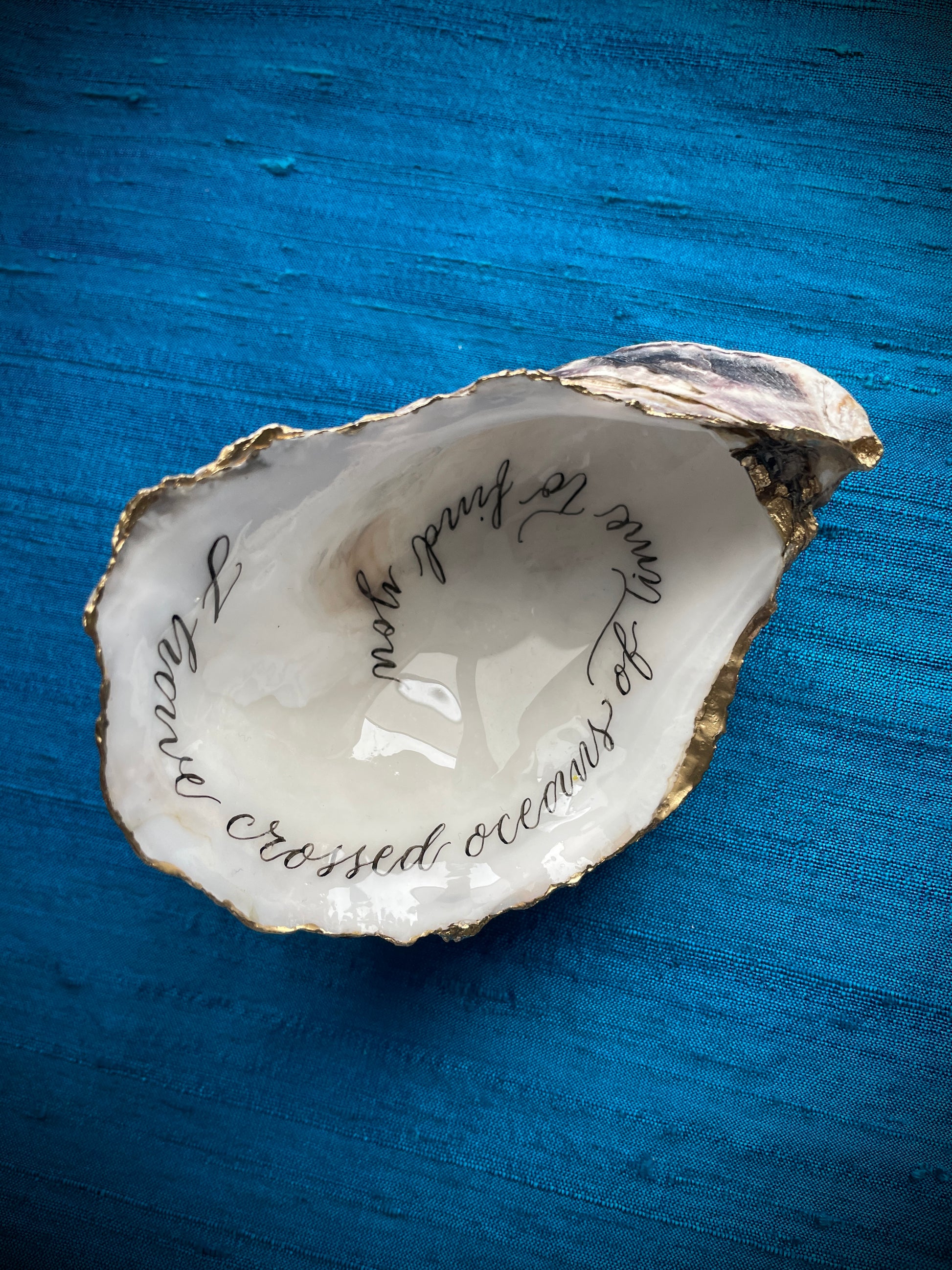 Cornish Oyster Shell Calligraphy
Made by: Julia Brooke - a word in your shell
'I have crossed oceans of time to find you'
The inside of this Cornish oyster shell has been beautifully hand written with a romantic message, delicately edged with gold leaf and the back lightly burnished with gold wax... perfect as a romantic gift.
The inside has been protected with clear uv stable resin making it smudge proof and moisture resistant, but not suitable for aquatic display.
Size: 9 cm x  x 6.5 cm / 3+1/2" x 2+1/2"