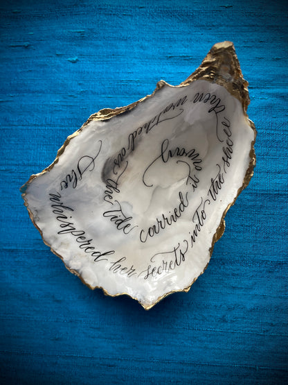 Cornish Oyster Shell Calligraphy
Made by: Julia Brooke - a word in your shell
'She whispered her secrets into the shell then watched as the tide carried it away'
The inside of this oyster shell has been beautifully hand written with a romantic message, edged with gold leaf and the back lightly burnished with gold wax, perfect as a romantic gift.
The inside is protected with a clear uv stable resin making it moisture resistant, but not for aquatic display.
Size: 11.5 cm x 7.5 cm /  / 4+1/2" x 3"