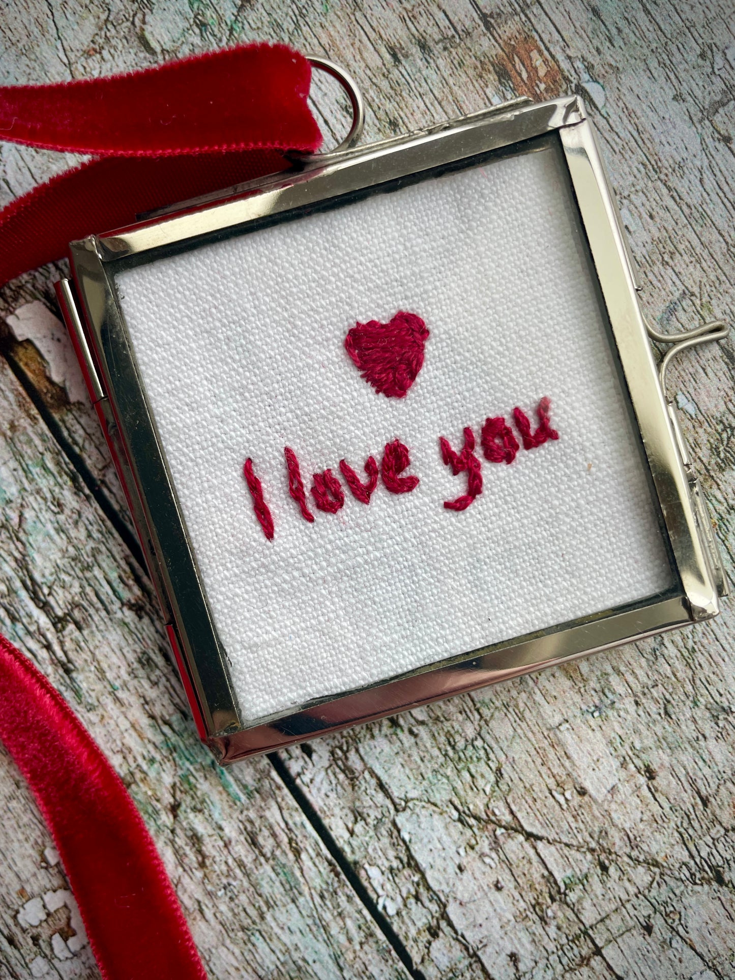 Romantic I Love You Keepsake

The words 'I love you' and a heart have been beautifully hand embroidered onto a piece of vintage French linen with deep red silk thread. It has been backed with a vintage floral cotton fabric, then placed inside a small glass and silver coloured metal frame with a deep red velvet hanging loop. Perfect as a small romantic keepsake.

Frame size approximately: 5 cm / 2" square.
Velvet loop length approximately: 15cm / 6" long.