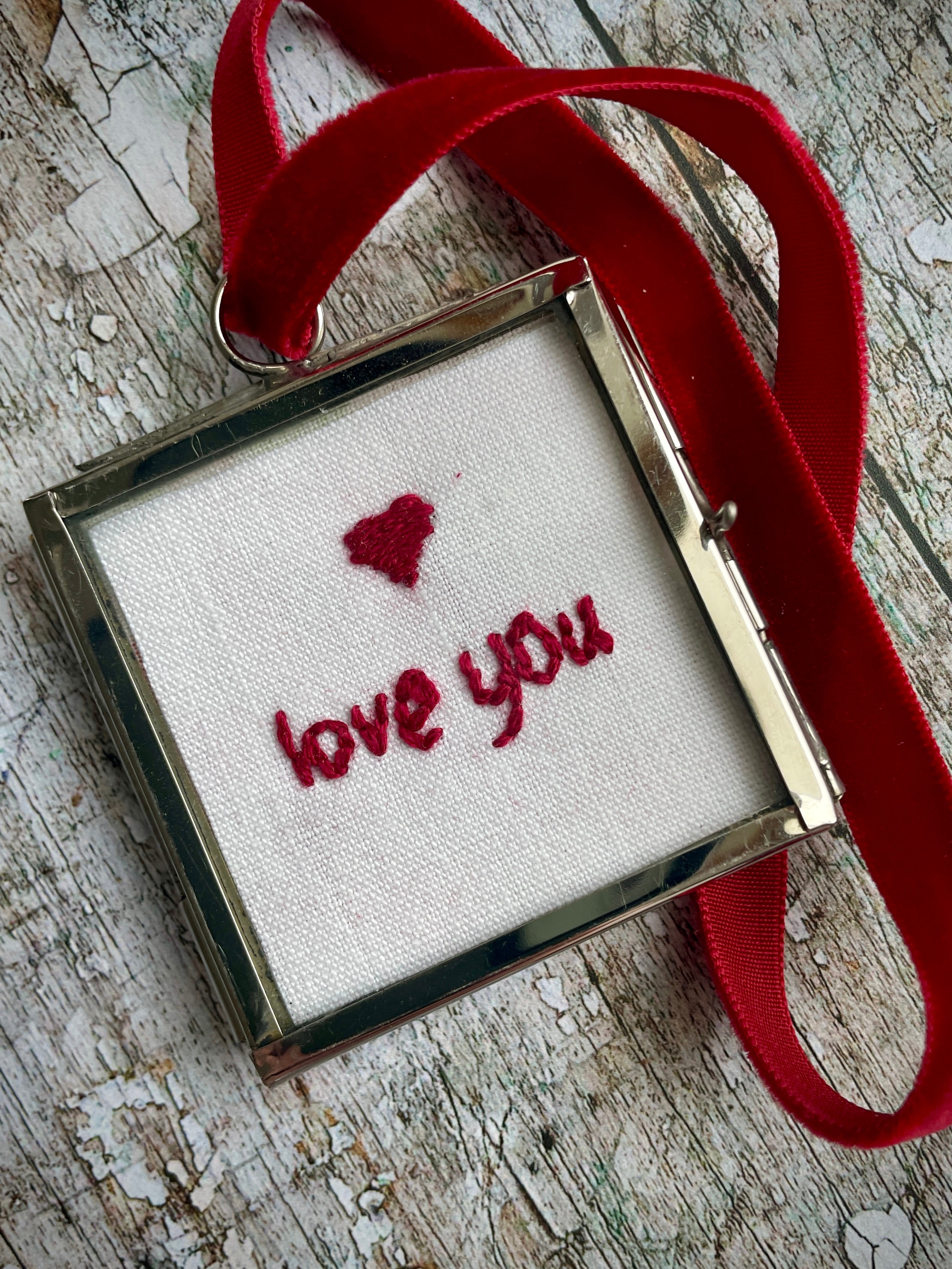 Romantic Love You keepsake

The words 'love you' and a heart have been beautifully hand embroidered onto a piece of vintage French linen with deep red silk thread. It has been backed with a vintage floral cotton fabric, then placed inside a small glass and silver coloured metal frame with a deep red velvet hanging loop. Perfect as a small romantic keepsake.
Frame size approximately: 5 cm / 2" square.
Velvet loop length approximately: 15cm / 6" long.