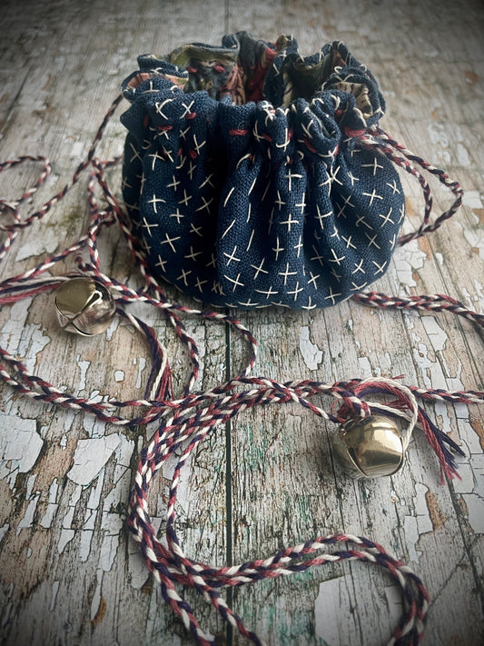 Small Hand Stitched Sashiko Pouch
Beautifully hand stitched drawstring pouch to hold your precious memories... a photograph, crystals, or finds from the beach. Made by hand stitching sashiko stitches on vintage Japanese dark indigo blue linen, lined with a pretty floral pattern cotton, hand printed. I then plaited 3 colours of matching cotton thread to make the drawstring cords ending in small silver colour bells. 
Pouch diameter when open approximately: 7+1/2" / 19 cm.
Cord lengths approx: 20" / 51 cm.