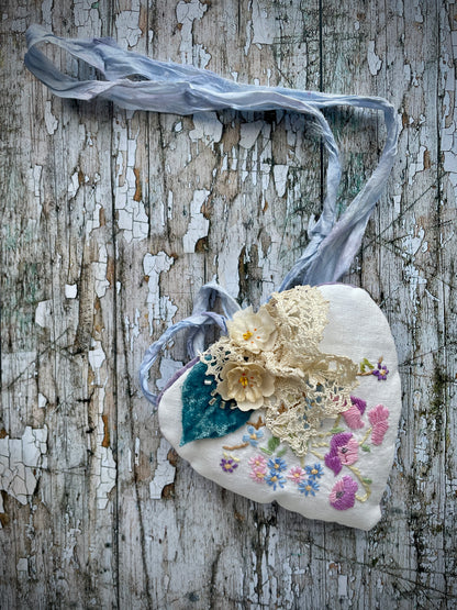 A beautiful one of a kind heart... made by hand stitching together vintage embroidered linen of pink, mauve, lavender and blue flowers, with vintage cream lace, linen flowers and a blue velvet leaf embellished with small silver bugle beads. The back is made of pale lavender velvet and the heart hangs with a loop of blue raw edged sari silk to wear around the neck or hang on the wall as a decoration. The inside of the heart has been gently filled with non-allergenic filling conforming to BS + CE  standards.