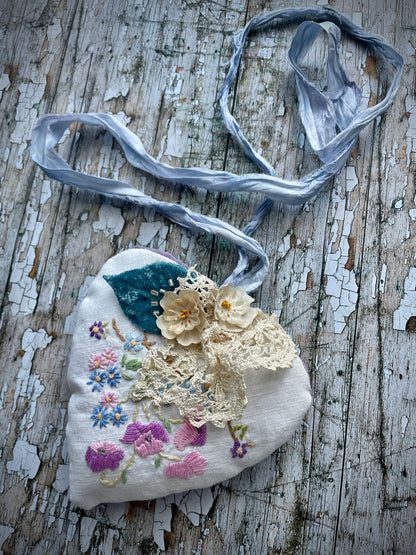 A beautiful one of a kind heart... made by hand stitching together vintage embroidered linen of pink, mauve, lavender and blue flowers, with vintage cream lace, linen flowers and a blue velvet leaf embellished with small silver bugle beads. The back is made of pale lavender velvet and the heart hangs with a loop of blue raw edged sari silk to wear around the neck or hang on the wall as a decoration. The inside of the heart has been gently filled with non-allergenic filling conforming to BS + CE  standards.