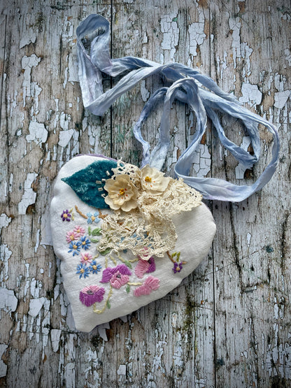 A beautiful one of a kind heart... made by hand stitching together vintage embroidered linen of pink, mauve, lavender and blue flowers, with vintage cream lace, linen flowers and a blue velvet leaf embellished with small silver bugle beads. The back is made of pale lavender velvet and the heart hangs with a loop of blue raw edged sari silk to wear around the neck or hang on the wall as a decoration. The inside of the heart has been gently filled with non-allergenic filling conforming to BS + CE  standards.