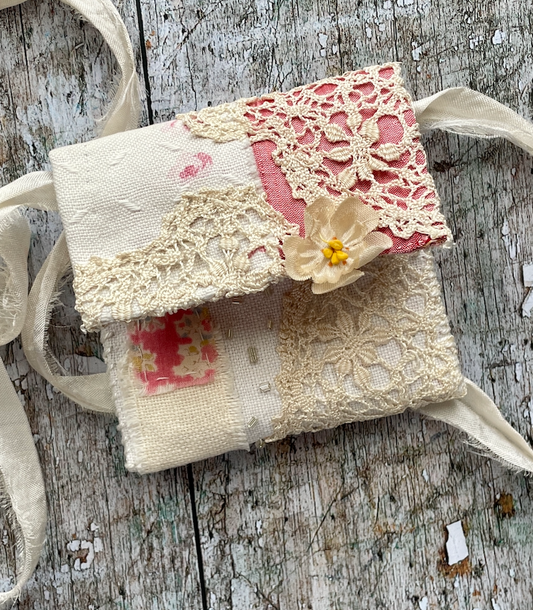 Small Hand Stitched Vintage Fabric Pouch

Beautifully hand stitched pouch to hold your precious memories... a photograph, crystals, a talisman or finds from the beach. It has been made by slow stitching together vintage French linens, lace, silk and quilting fabrics in shades of cream and white, lined with a pretty pink vintage paisley cotton, then embellished with small silver bugle beads and a vintage fabric flower. The pouch has a simple fold over top, with a raw edged cream sari silk cord.